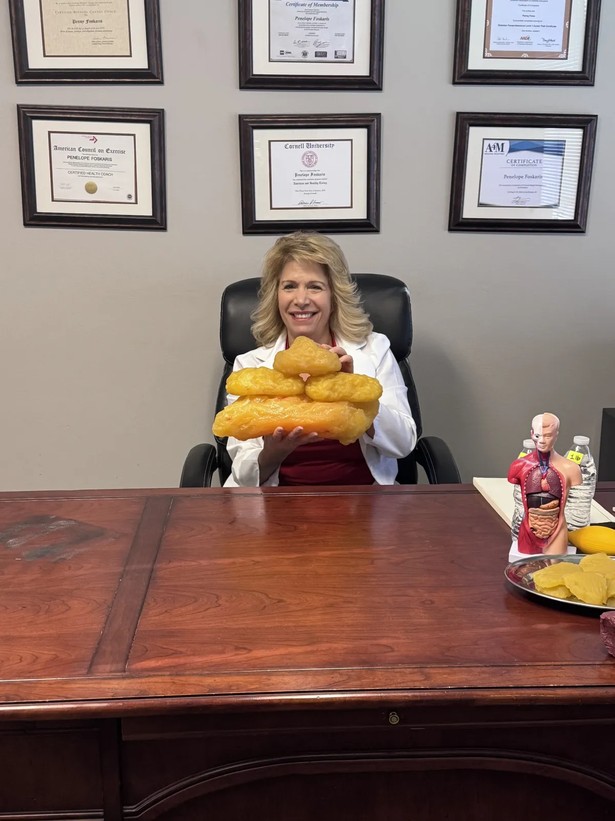 Penny Foskaris in her clinical office with certifications, credentials, and body composition model